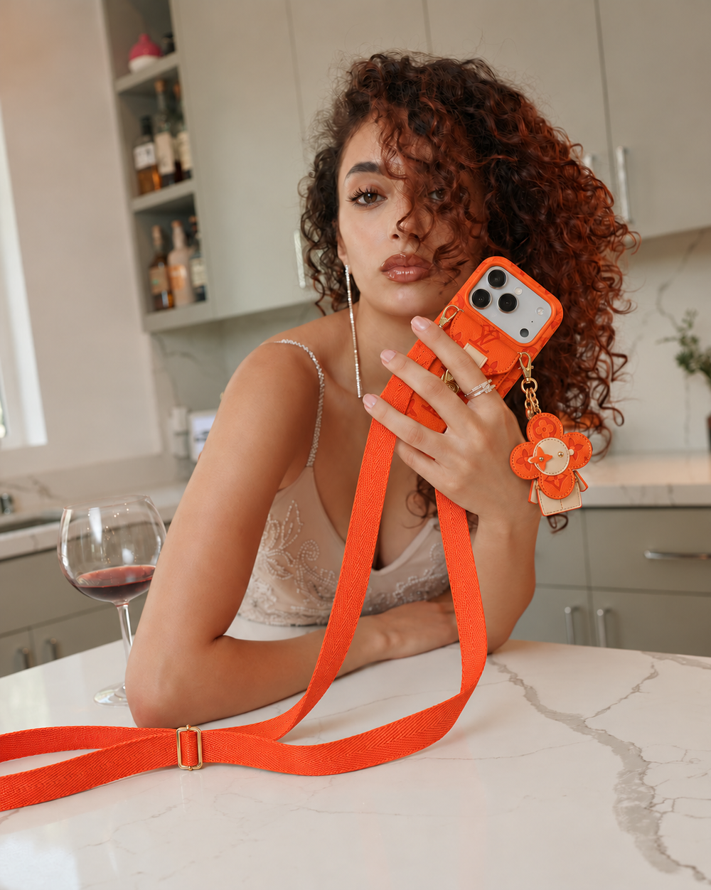 Orange monogram crossbody iPhone case with pocket and flower charm, lifestyle scene 1